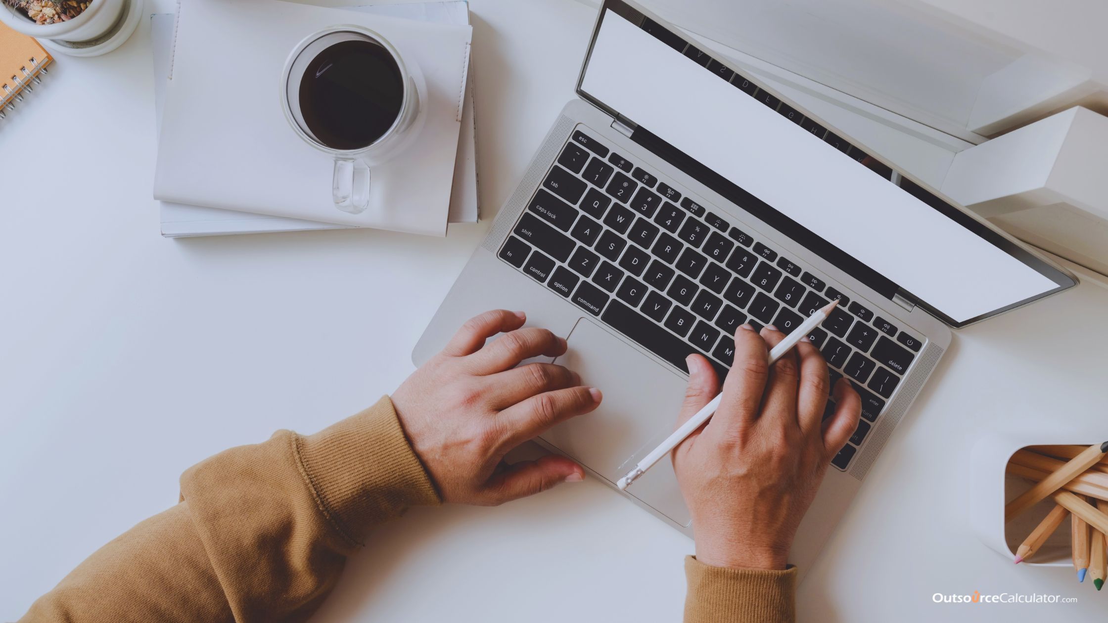 a remote employee holding a pencil while working on a laptop with a coffee beside it.